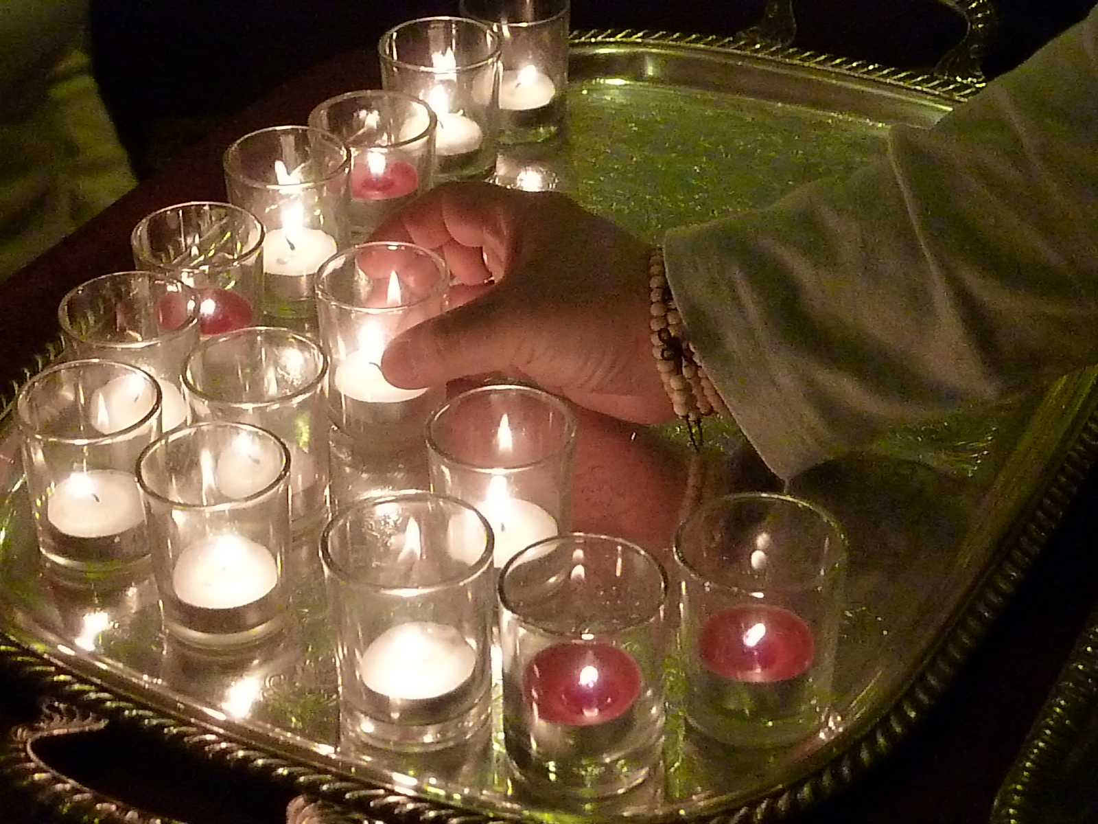 A hand places a lit candle in the middle of a silver tray of other candles.